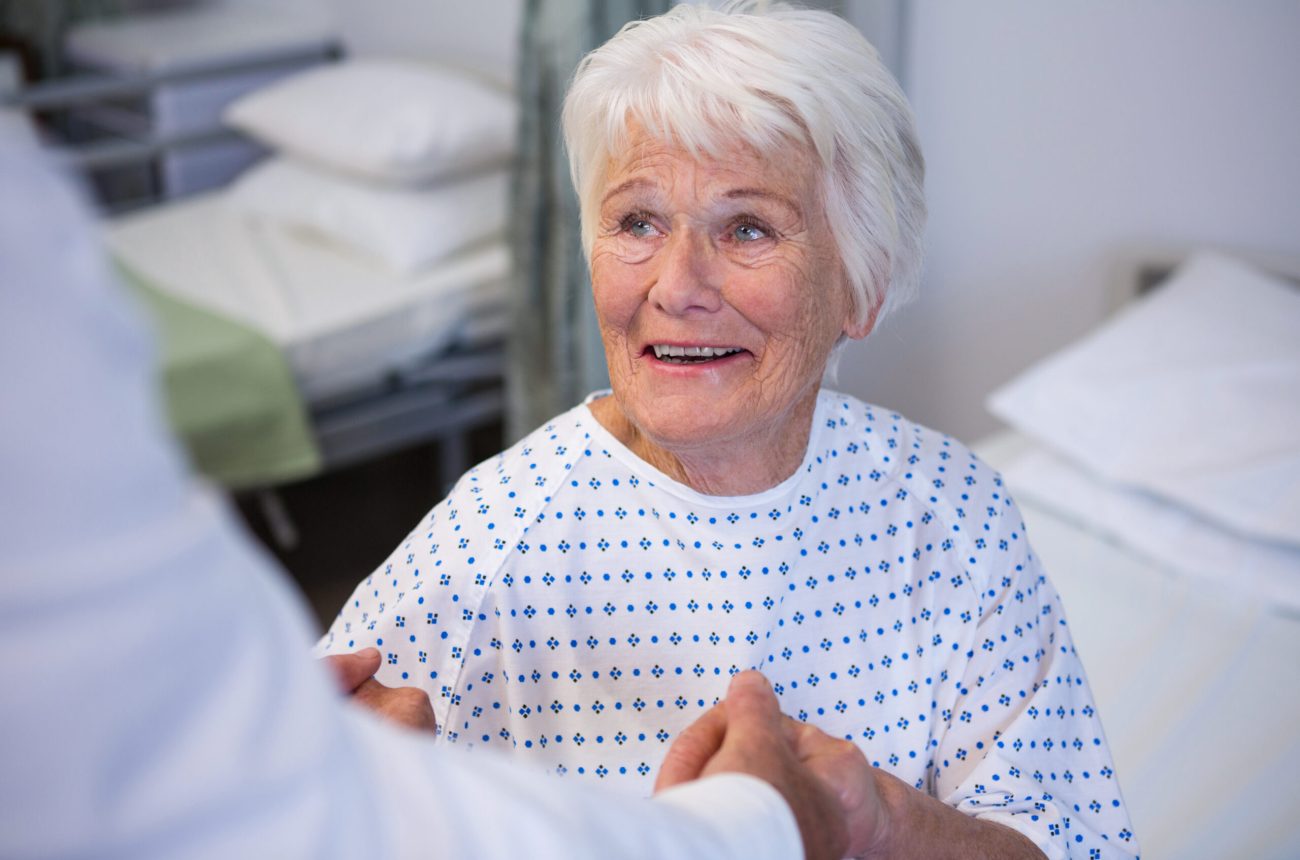 Doctor consoling senior patient in ward at hospital